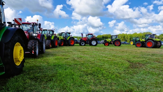 Krāsaini traktori pusaplī, uz zaļa lauka