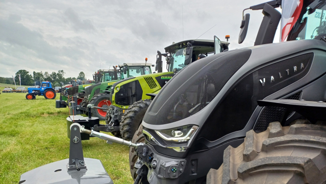 Krāsainu traktoru rinda uz zaļa lauka