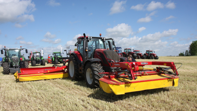 Krāsaini traktori ar agregātiem sastājušies uz lauka nesistemātiski viens aiz otra