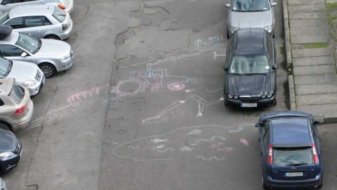 Starp automašīnām uz ielas uzzīmēti lauki un cilvēks tajos