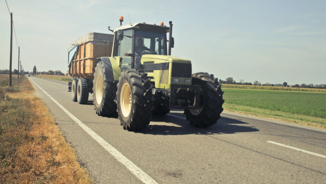 Traktors ar piekabi brauc pa asfaltētu ceļu