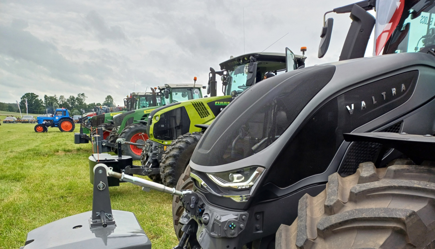 Krāsainu traktoru rinda uz zaļa lauka