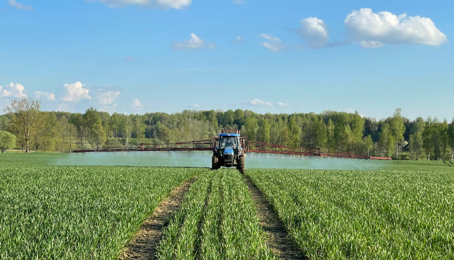 Traktors ar pieāķētu augu aizsardzības līdzekļu lietošanas iekārtu smidzina barības vielas zaļam labības laukam