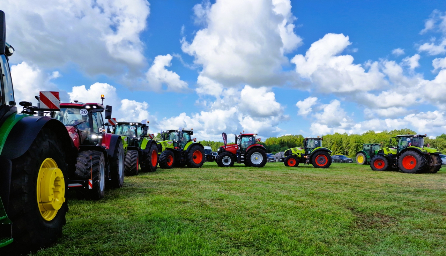 Krāsaini traktori pusaplī, uz zaļa lauka