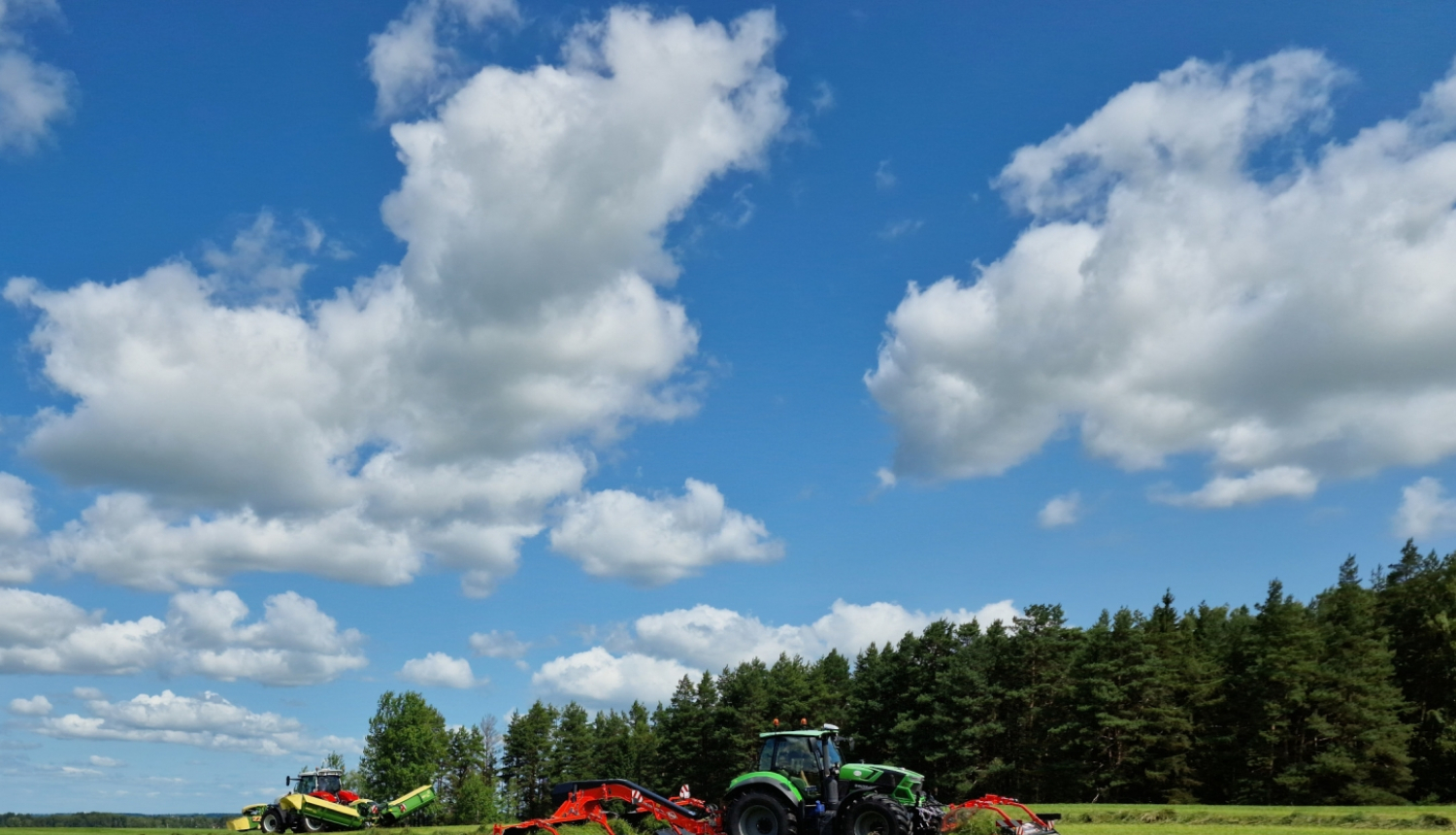 Traktortehnika uz lauka pļauj un vāc zāli, sienu