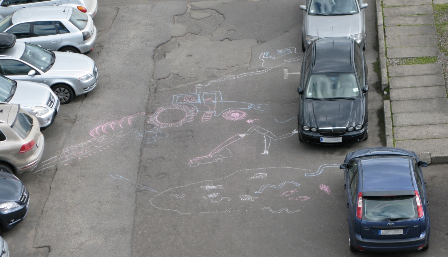 Starp automašīnām uz ielas uzzīmēti lauki un cilvēks tajos