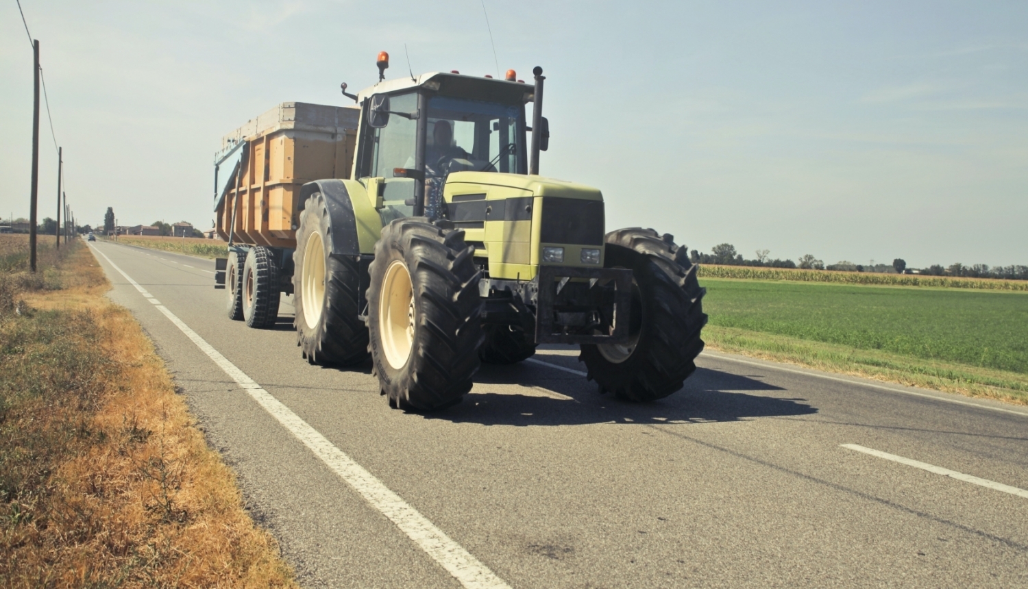 Traktors ar piekabi brauc pa asfaltētu ceļu
